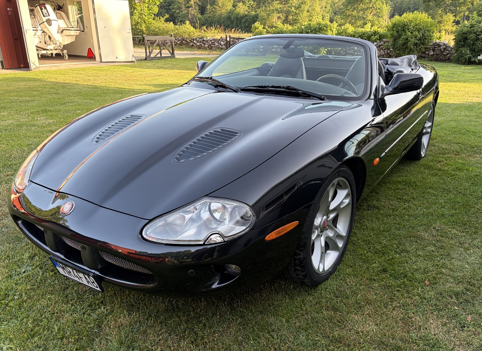Svart sportbil av märket Jaguar XKRmed blank kaross, framlyktor och motorhuv på gräsmatta framför garage och grönskande trädgård.